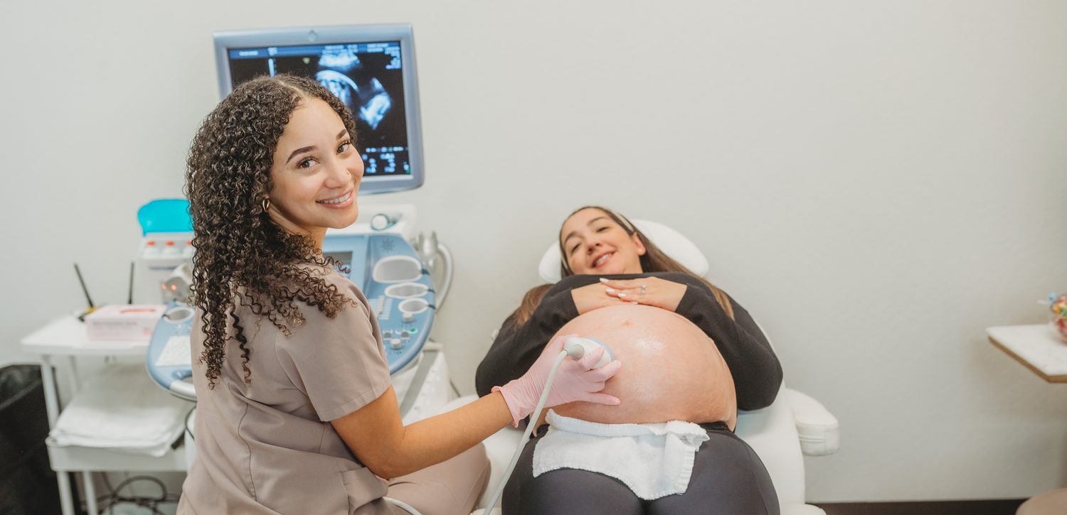 Ericka scanning an expectant mother in the Sweet 3D Baby studio, with the ultrasound image on the screen behind them.